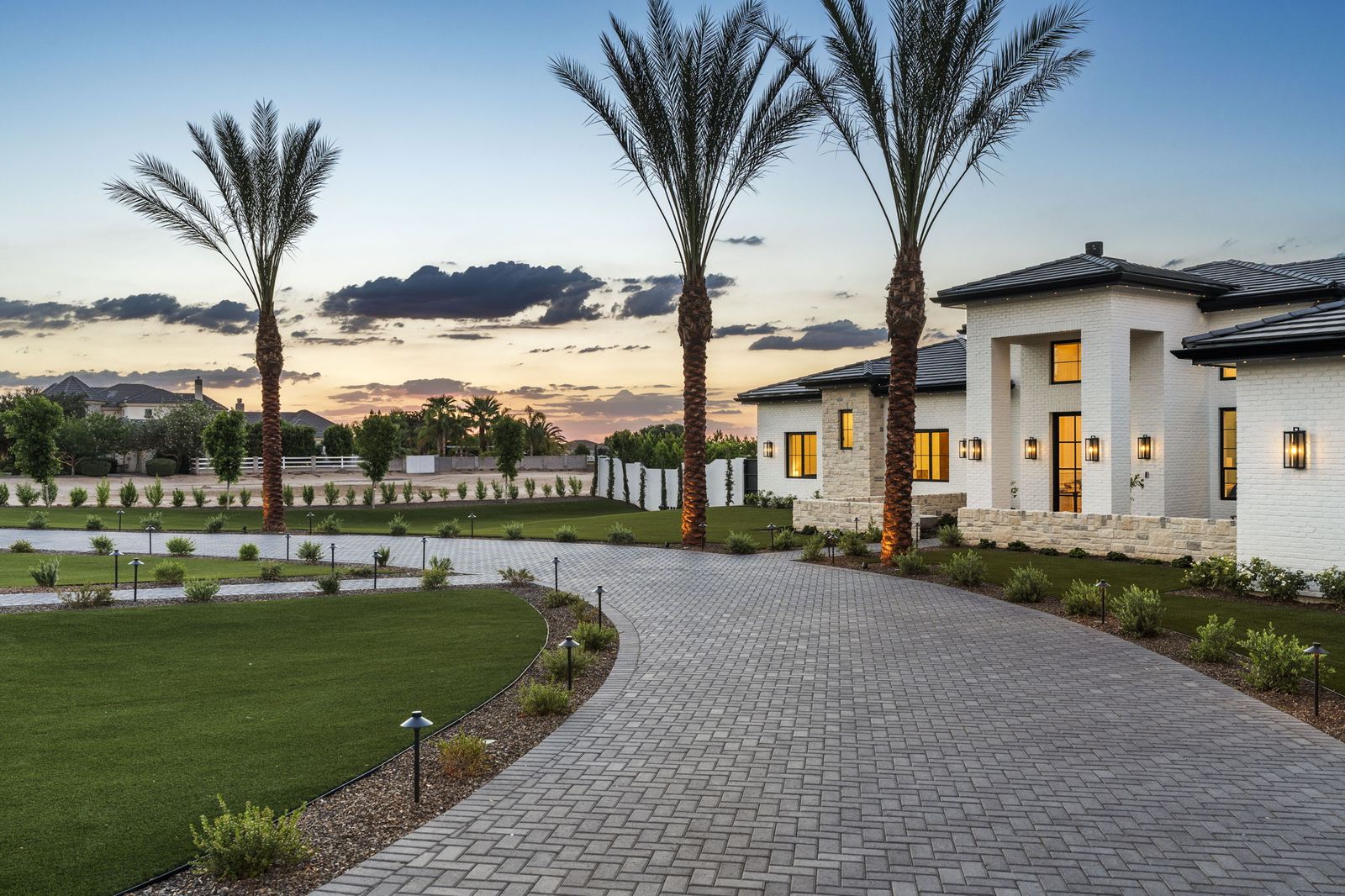Twilight view of the palm-lined paver driveway at the Pegasus Pkwy Residence, Queen Creek AZ