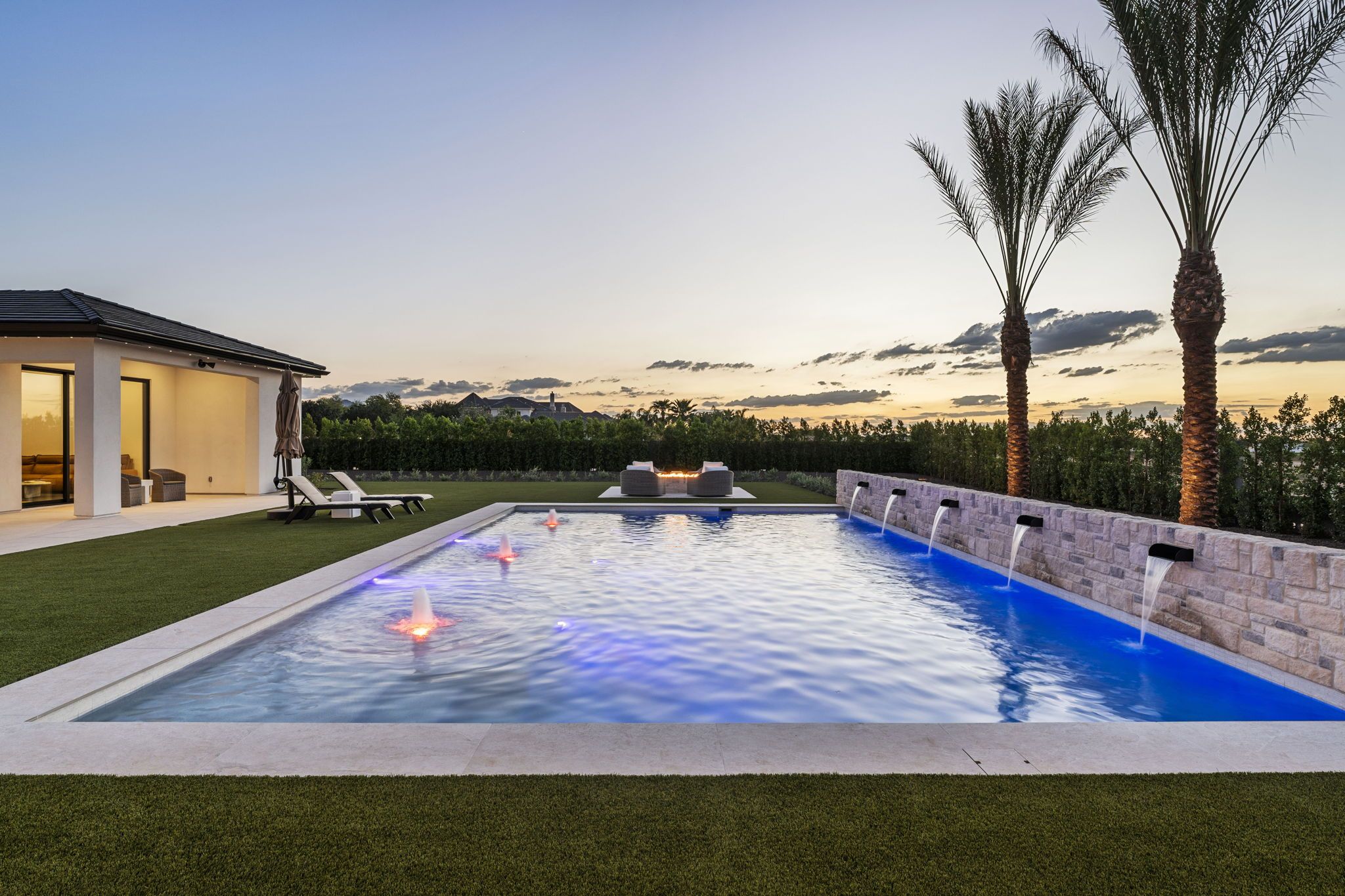 Resort pool with lighted water features at dusk at the Pegasus Pkwy Residence, a custom home by Prestige Build Co. in Queen Creek AZ